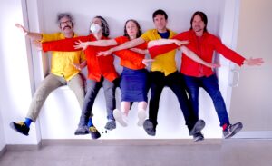 five white people are sitting on a ledge wearing bright colors and interlocking arms with their feet in the air